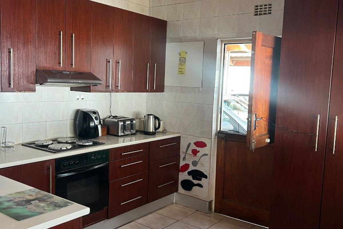 A functional kitchen featuring dark wood cabinetry, built-in oven, gas hob, extractor fan, and tiled flooring with direct access to the exterior.