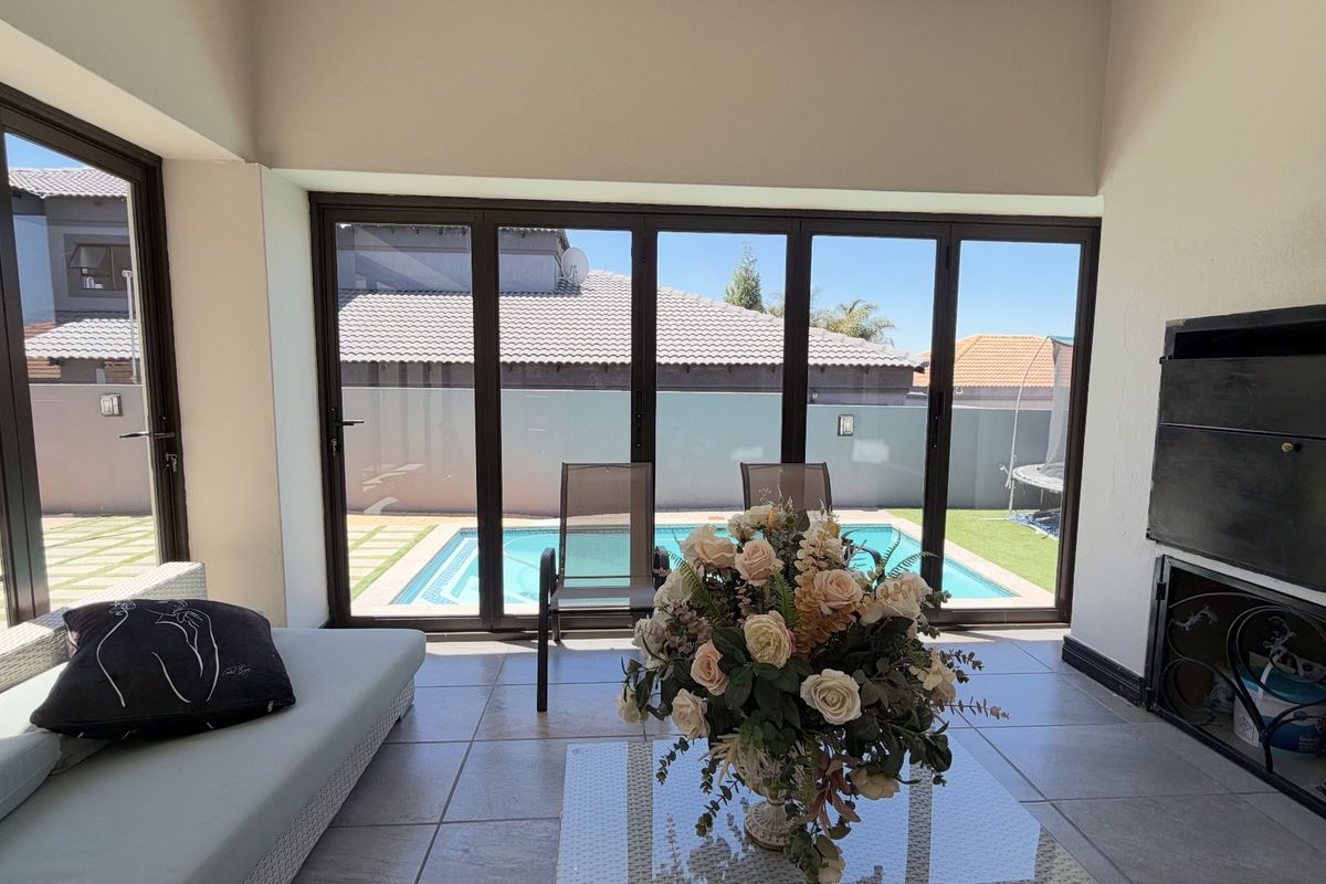 Bright living area featuring large aluminium stackable doors that open onto a pool patio, complemented by a built-in fireplace and tiled flooring.