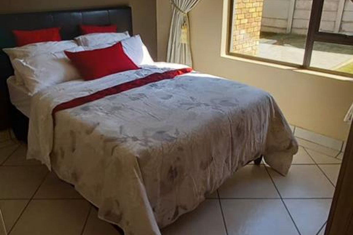 A well-lit bedroom featuring tiled flooring, a large window with curtain tracks, and a neutral color palette.