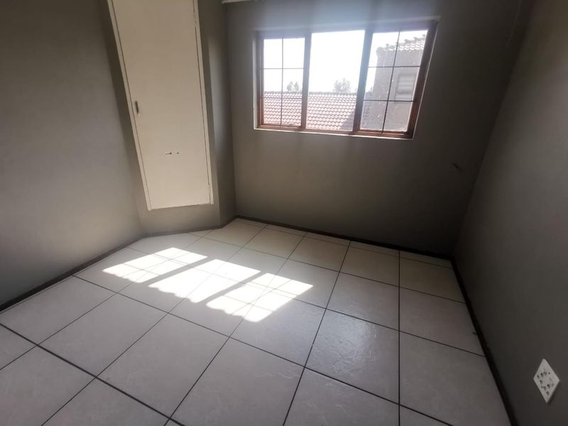 An empty bedroom featuring tiled flooring, a built-in cupboard, and natural light through a window with security bars.