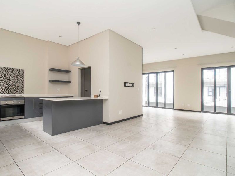 Spacious open-plan living and kitchen area featuring modern grey cabinetry, stone countertops, tiled flooring, and large sliding doors leading to the exterior.