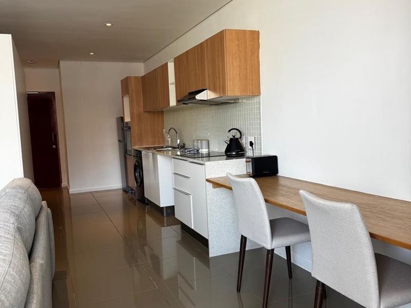 Modern open-plan kitchen featuring sleek cabinetry, stone countertops, mosaic backsplash, and integrated appliances, seamlessly flowing into the living area with polished tiled floors.