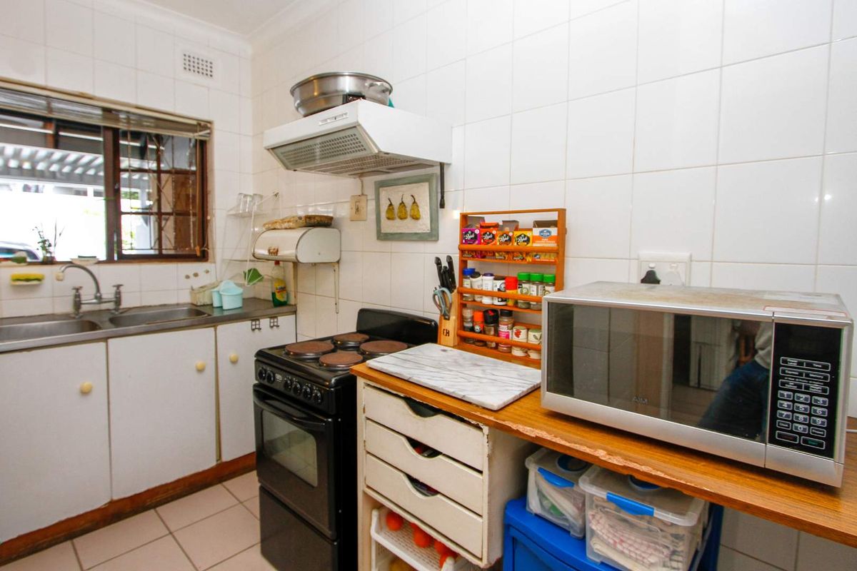 A compact kitchen featuring tiled walls, a built-in stove with extractor fan, and a stainless steel sink with window view.