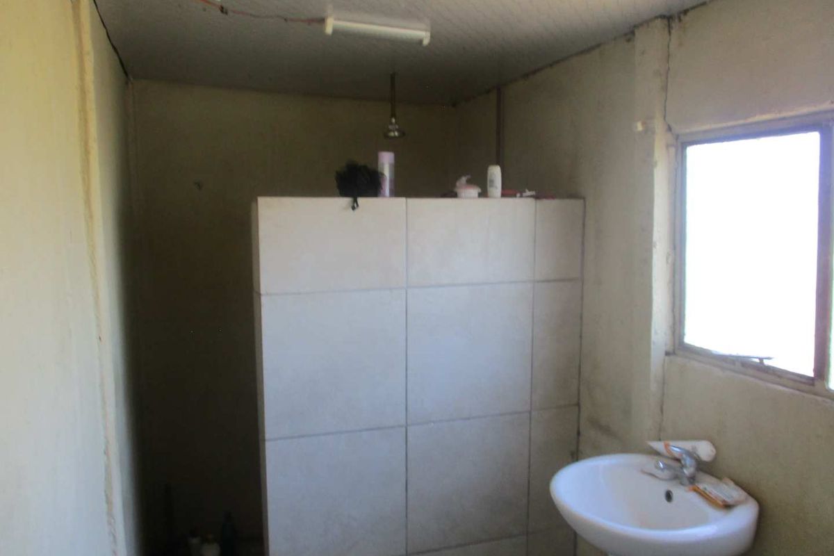 A basic bathroom featuring a pedestal basin and a tiled shower partition, requiring significant renovation and cosmetic updates to improve its condition.