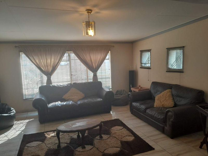 A living room featuring tiled flooring, security bars on the windows, and a central ceiling light fixture.