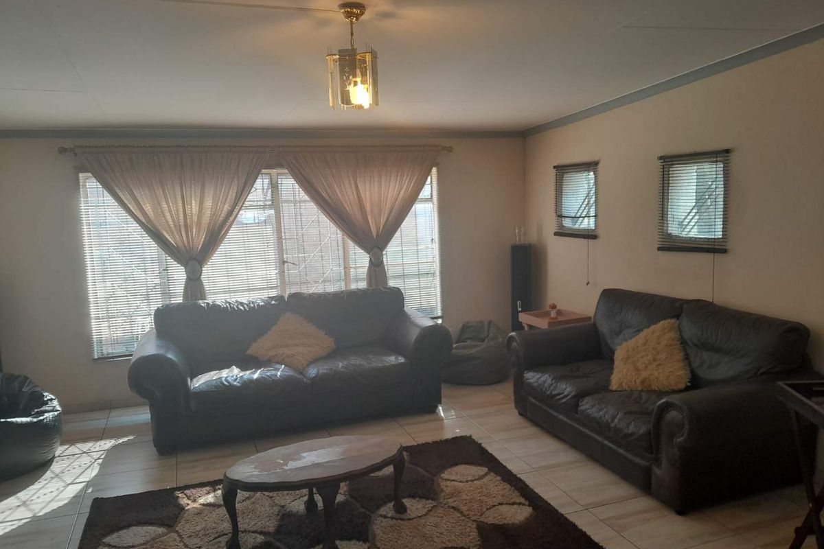 A living room featuring tiled flooring, security bars on the windows, and a central ceiling light fixture.