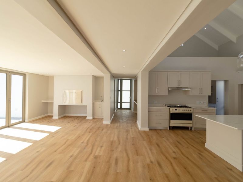 Spacious open-plan living and kitchen area featuring modern cabinetry, a gas stove, laminate flooring, and large glass doors leading to the exterior.