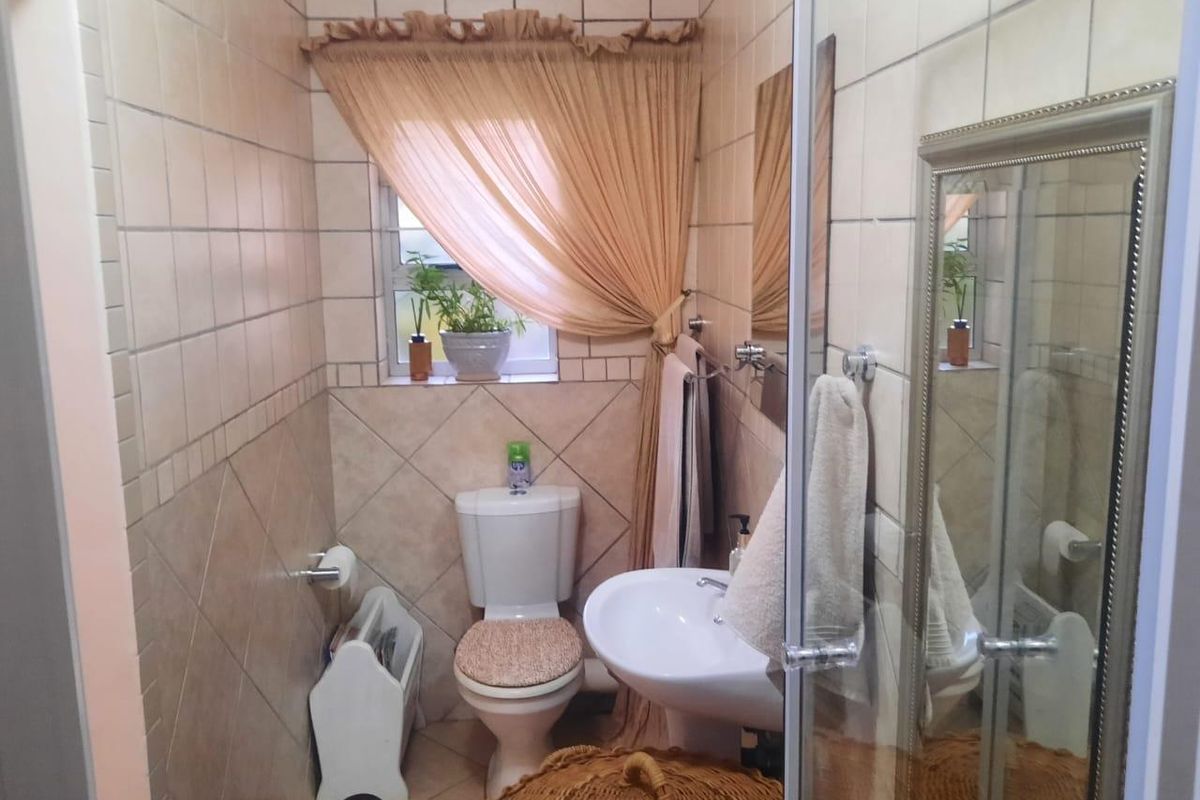 A compact bathroom featuring a pedestal basin, toilet, and shower enclosure with neutral ceramic wall and floor tiling.