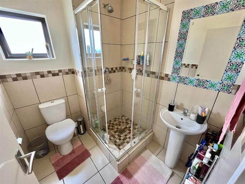 Compact bathroom featuring a corner shower enclosure, pedestal basin, and toilet with neutral wall and floor tiling.
