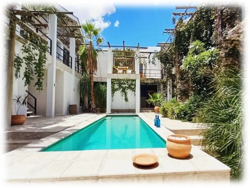 A serene outdoor pool area featuring a rectangular swimming pool, tiled surround, and architectural pergola structures with climbing greenery.