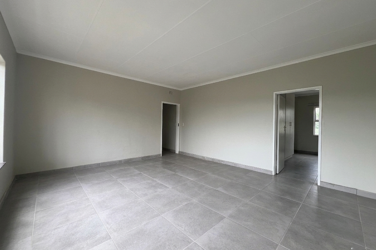 A spacious, empty living area featuring neutral wall tones and modern grey floor tiles, providing a clean and versatile blank canvas.