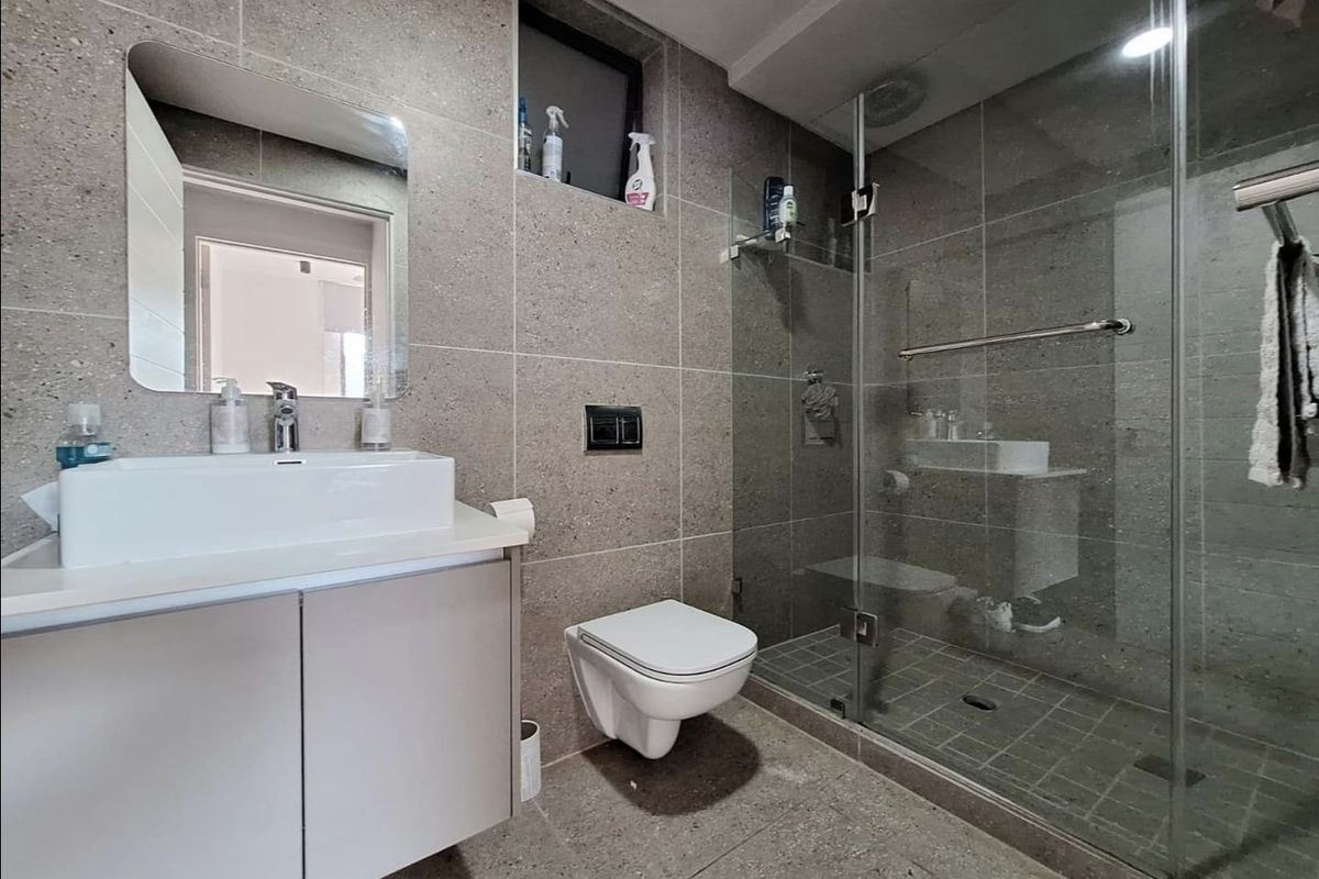 Modern bathroom featuring a wall-mounted toilet, glass-enclosed shower, vessel sink with vanity cabinet, and contemporary grey floor-to-ceiling tiling.