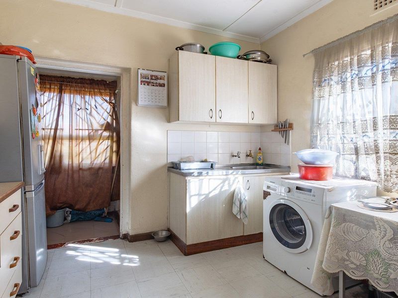 A functional kitchen featuring built-in cabinetry, a stainless steel sink, and tiled flooring, offering potential for modernization and cosmetic updates.