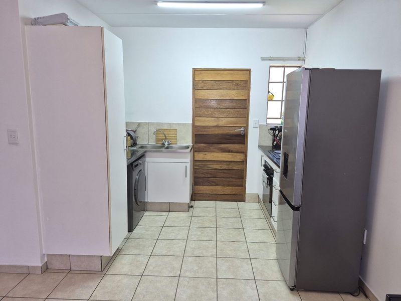 A functional kitchen featuring tiled flooring, built-in cabinetry, a stainless steel sink, and a solid timber door leading to an adjacent area.