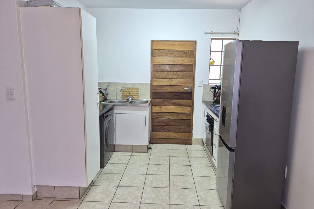 A functional kitchen featuring tiled flooring, built-in cabinetry, a stainless steel sink, and a solid timber door leading to an adjacent area.