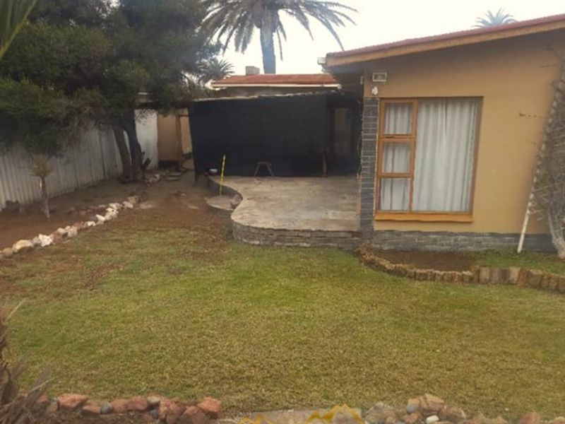 Rear view of the property featuring a paved patio area, established lawn, and stone garden borders.