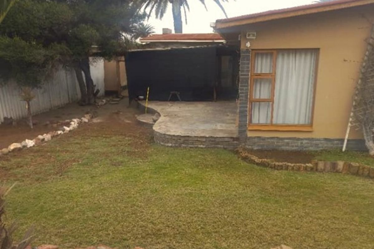 Rear view of the property featuring a paved patio area, established lawn, and stone garden borders.