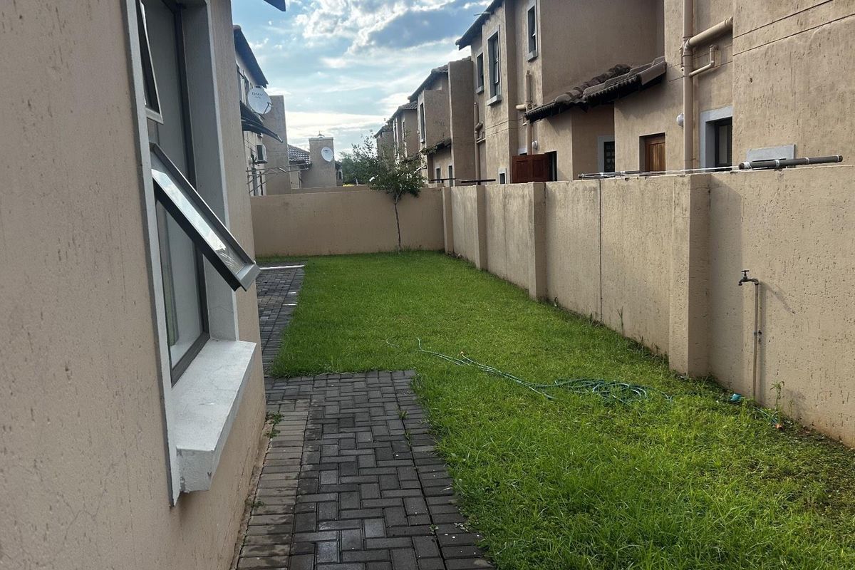 A private rear garden area featuring a paved walkway, a small lawn, and a high boundary wall for privacy.