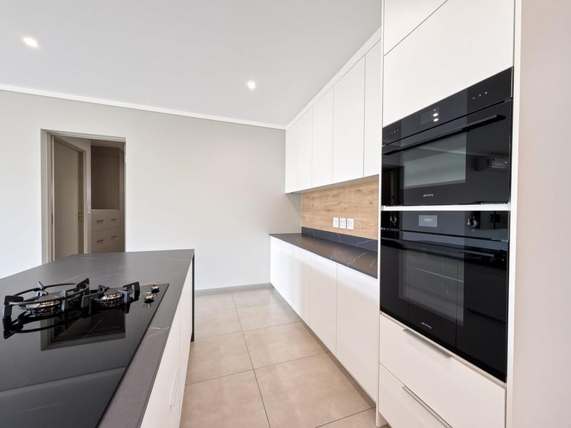 Modern kitchen featuring sleek white cabinetry, dark stone countertops, integrated Smeg appliances, and a central island with a gas hob.