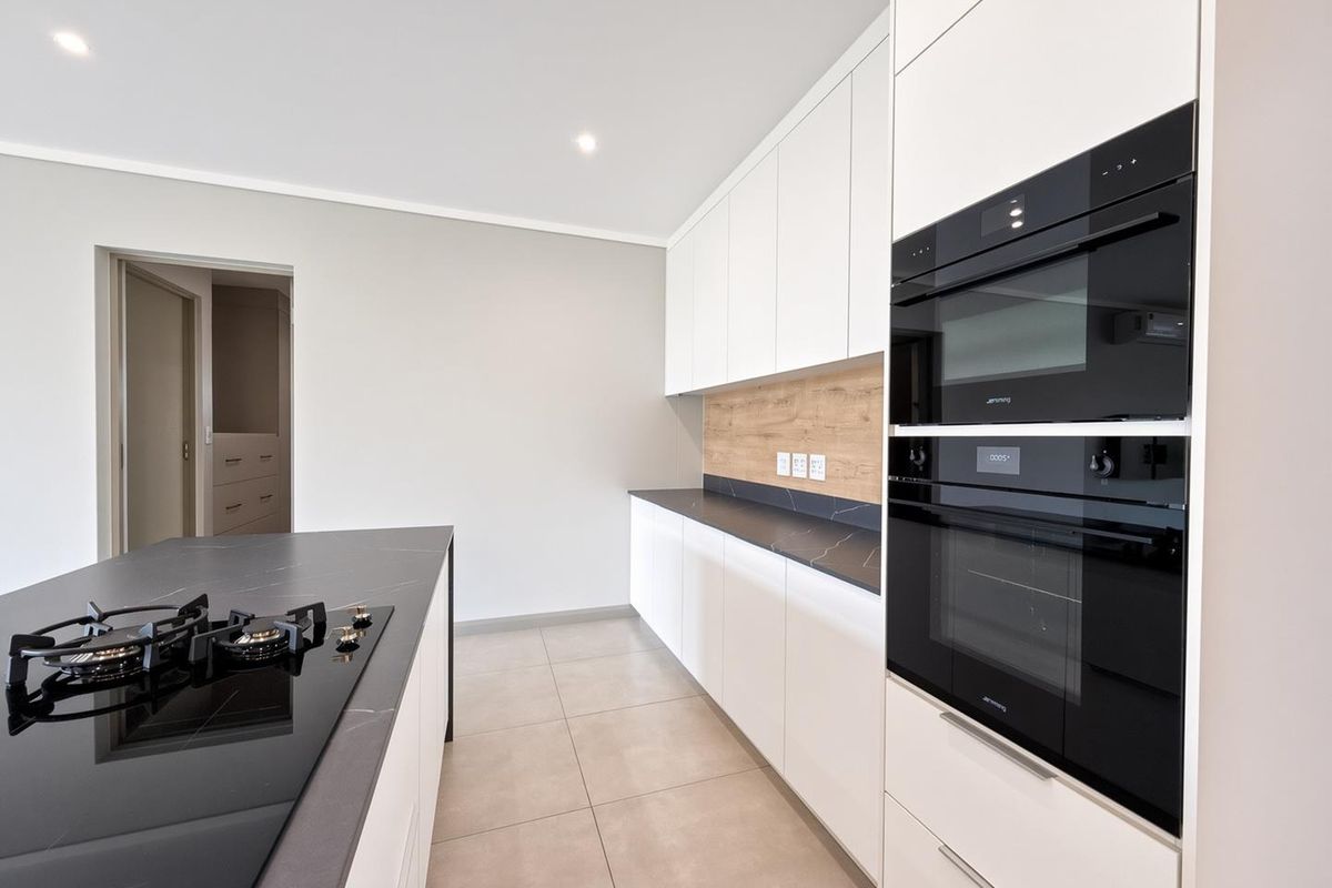 Modern kitchen featuring sleek white cabinetry, dark stone countertops, integrated Smeg appliances, and a central island with a gas hob.
