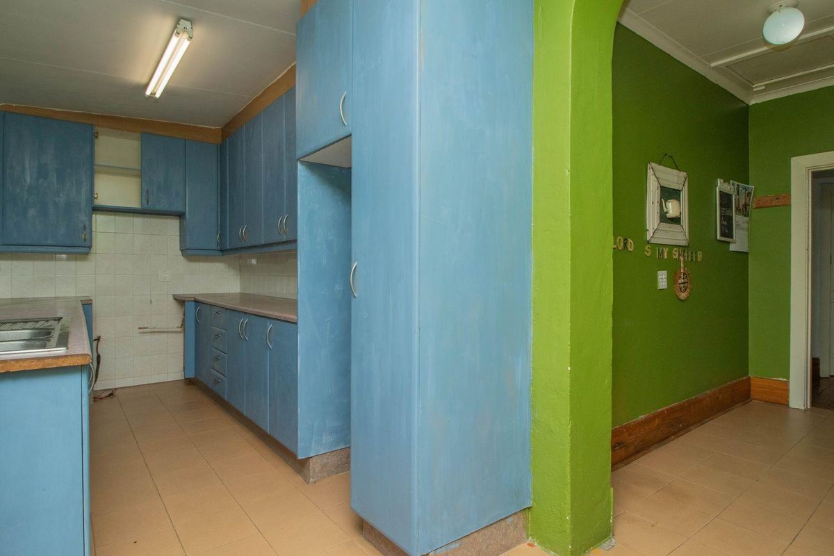 A functional kitchen area featuring blue cabinetry, tiled flooring, and an adjacent green-painted hallway with an arched entryway.