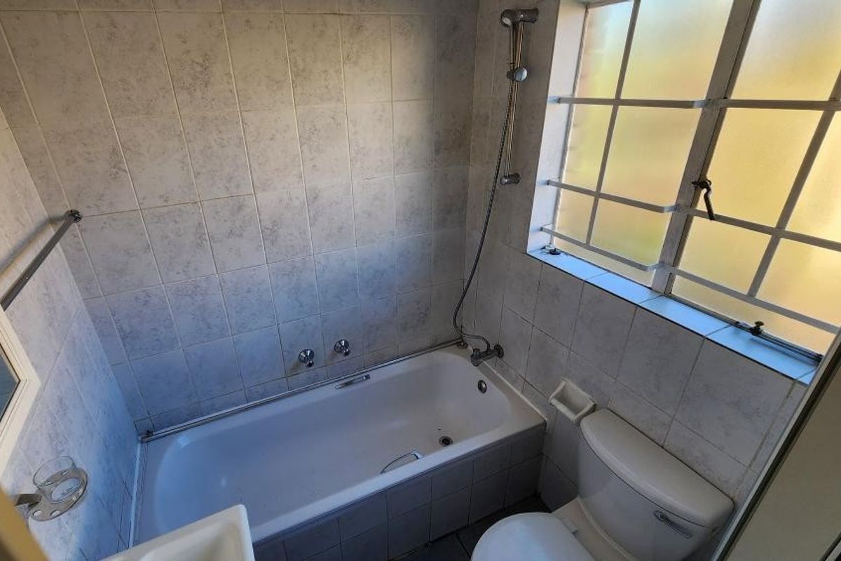A functional bathroom featuring a bathtub with shower mixer, toilet, and tiled walls, offering a clean but dated aesthetic ready for modernization.