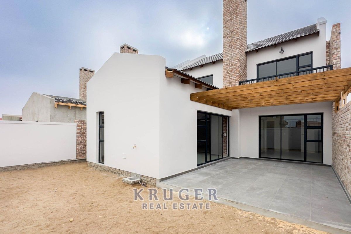 Rear view of a modern townhouse featuring a tiled patio, timber pergola, and sliding glass doors leading into the living area.