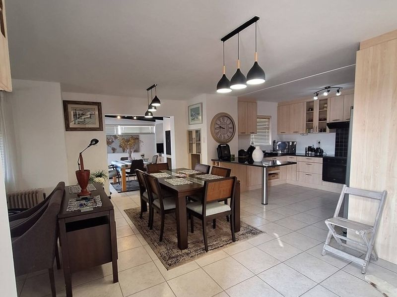Spacious open-plan living and dining area featuring tiled floors, modern pendant lighting, and a functional kitchen with built-in cabinetry and integrated appliances.