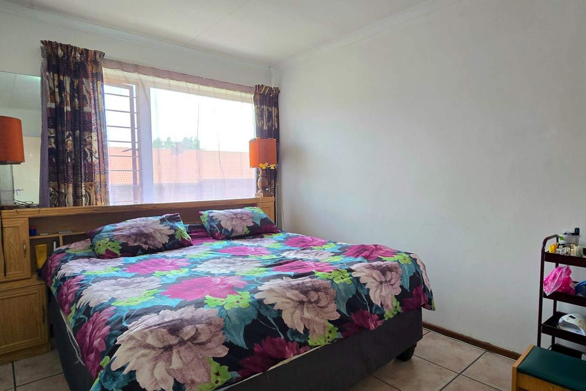 A standard bedroom featuring tiled flooring, a built-in headboard unit, and a window with security bars.