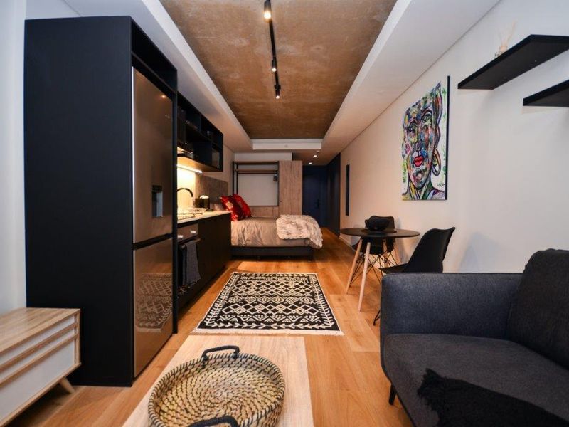 Modern open-plan studio apartment featuring a sleek integrated kitchen, hardwood flooring, and a unique exposed concrete ceiling design with track lighting.