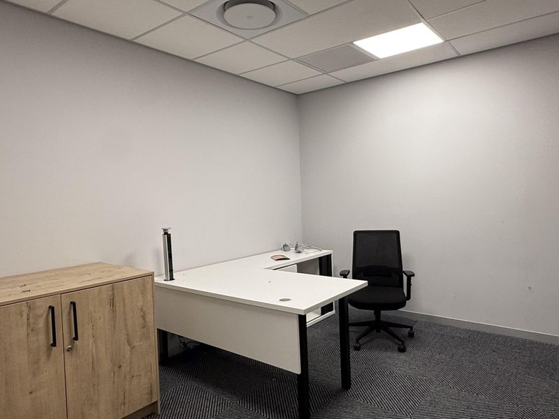 A clean, professional office space featuring neutral walls, carpeted flooring, and a suspended ceiling with integrated lighting and air conditioning.