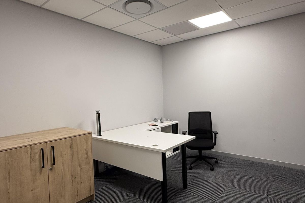A clean, professional office space featuring neutral walls, carpeted flooring, and a suspended ceiling with integrated lighting and air conditioning.