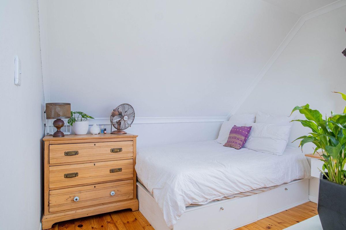 A cozy bedroom featuring a sloped ceiling, timber flooring, and a built-in bed base with storage drawers.