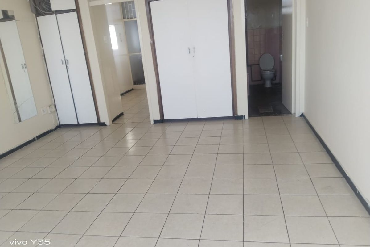 An empty bedroom featuring built-in cupboards, tiled flooring, and direct access to an en-suite bathroom.