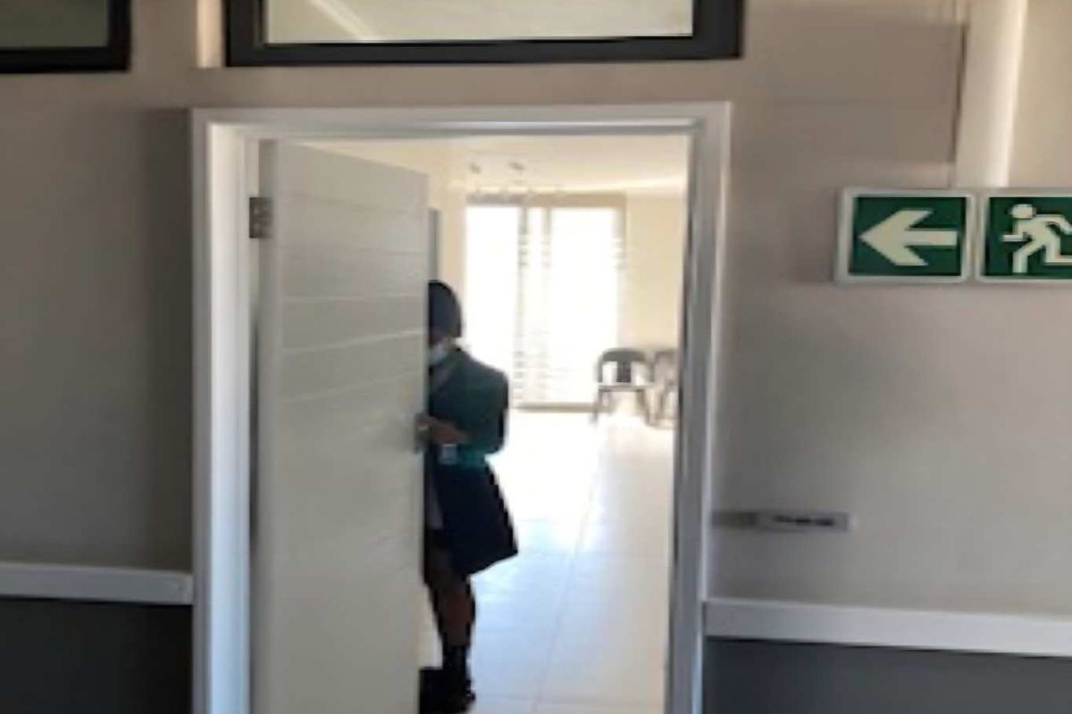 A view of a hallway featuring an emergency exit sign and a doorway leading into an adjacent room.