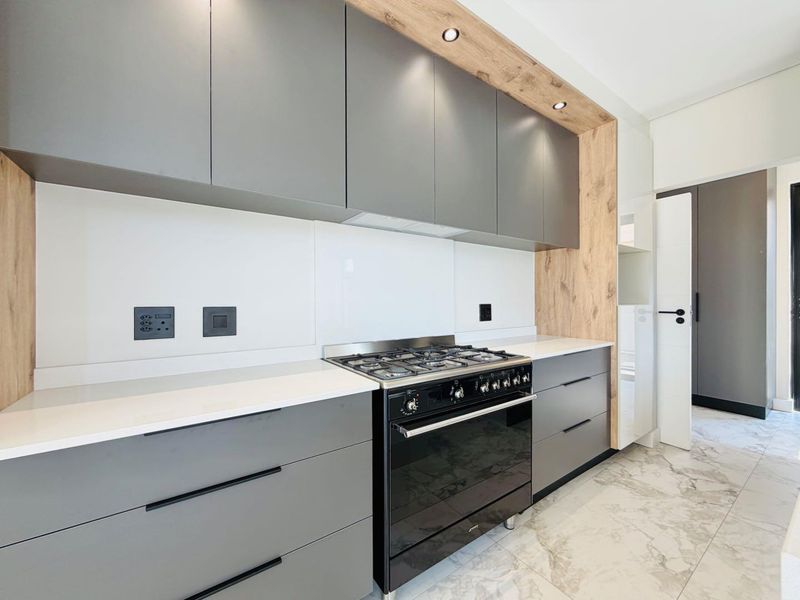 Modern kitchen featuring sleek grey cabinetry, wood-look accents, stone countertops, and a high-end gas stove with oven.
