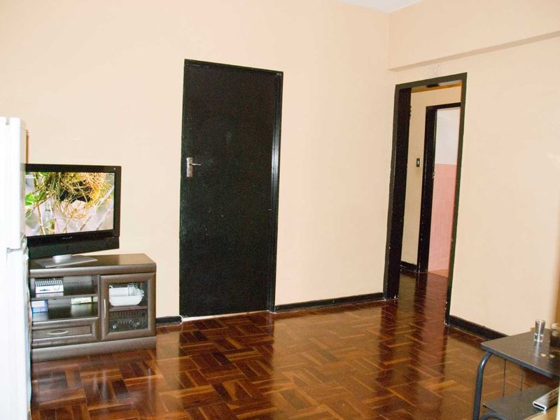 A living area featuring dark parquet flooring and internal doors, showing signs of wear and dated finishes.