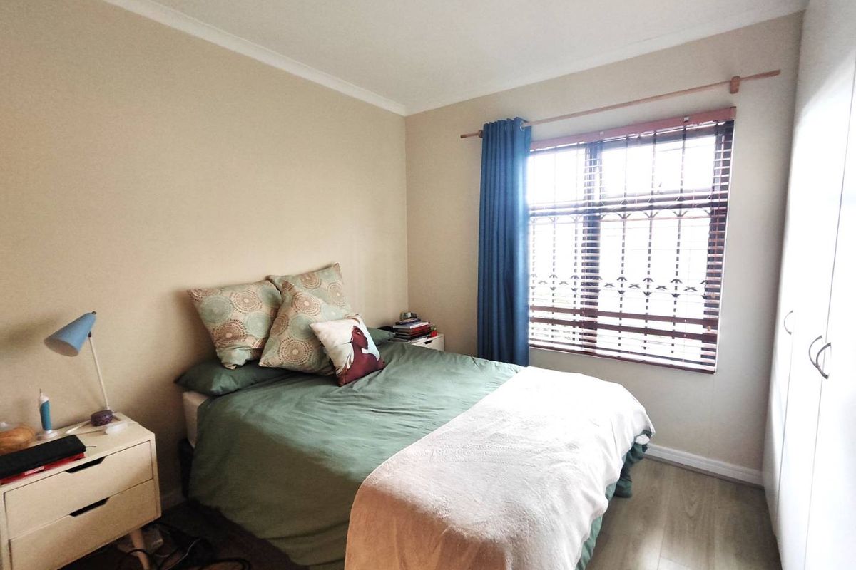 A functional bedroom featuring laminate flooring, a built-in wardrobe, and a window fitted with security bars for added peace of mind.