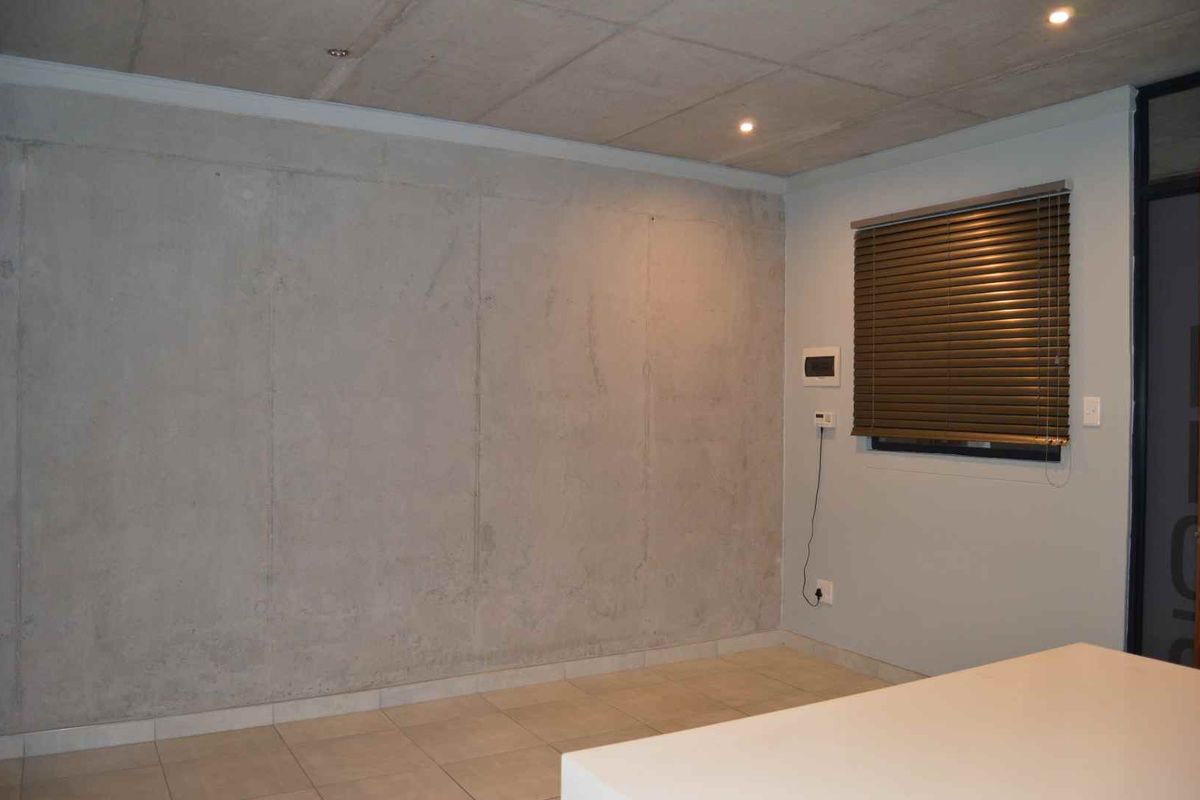Modern living area featuring an exposed concrete ceiling and feature wall, tiled flooring, and recessed lighting, offering a contemporary industrial aesthetic.