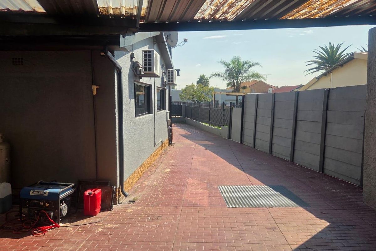A paved side driveway area featuring a covered carport structure, perimeter walling, and external air conditioning units.