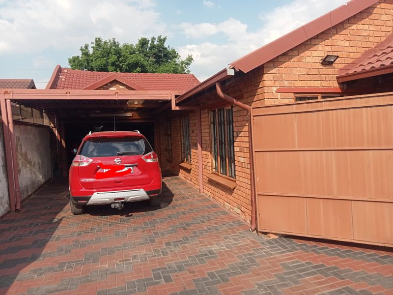 Front exterior view of a face brick house featuring a paved driveway, carport, and secure gated entrance.