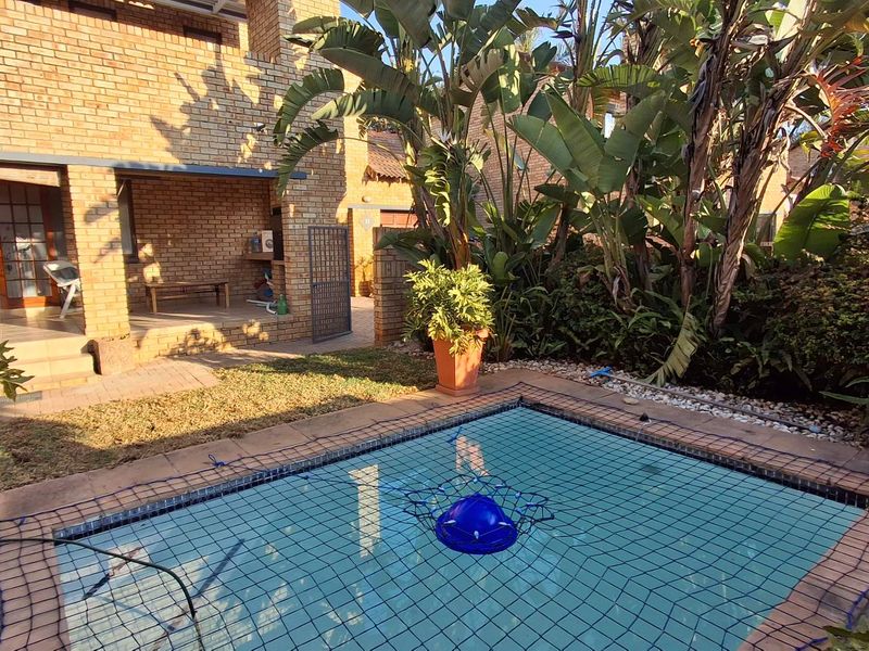 A private backyard featuring a swimming pool with a safety net, adjacent to a brick-built townhouse with a covered patio area.