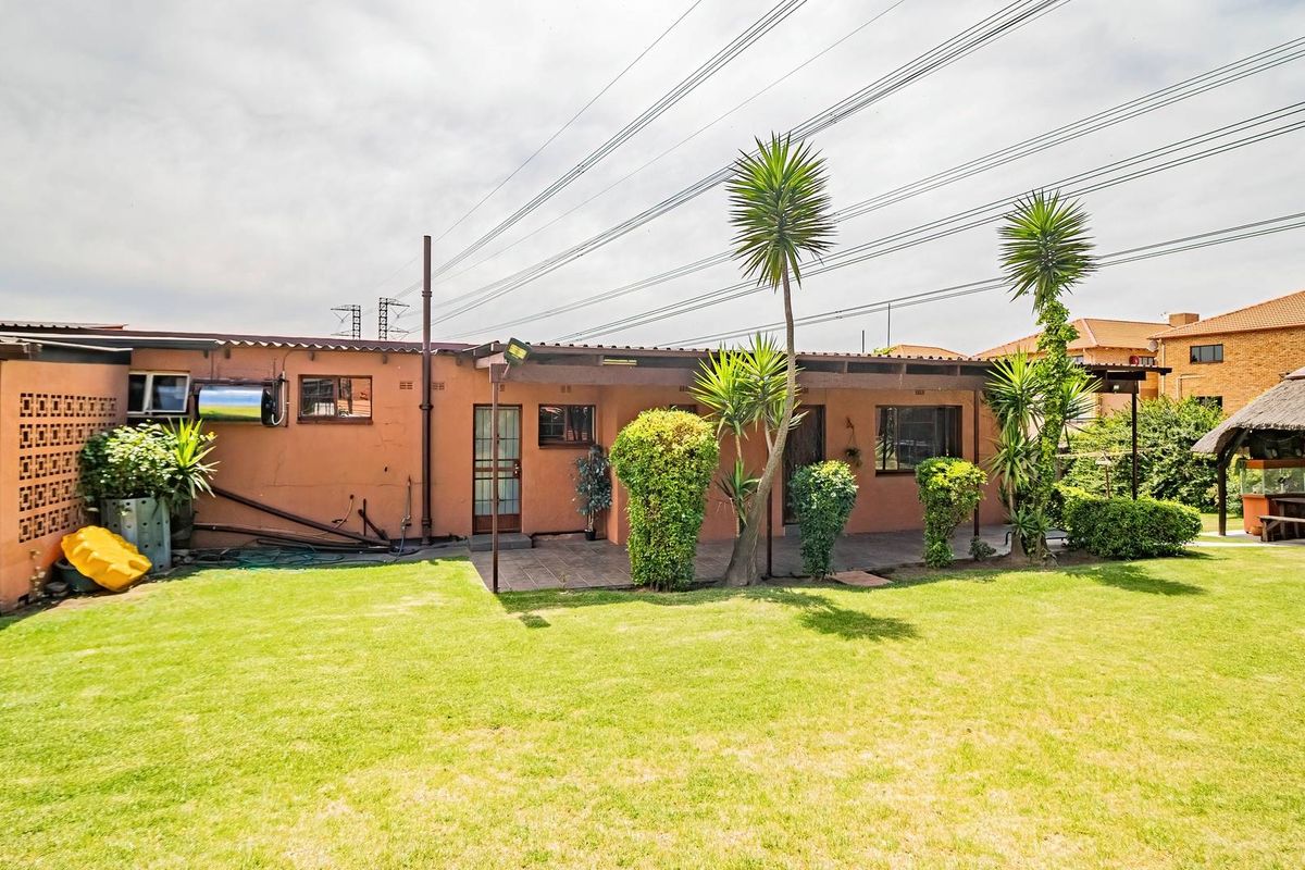 Rear view of the property featuring a covered patio, a thatched lapa, and a spacious lawn area with established landscaping.