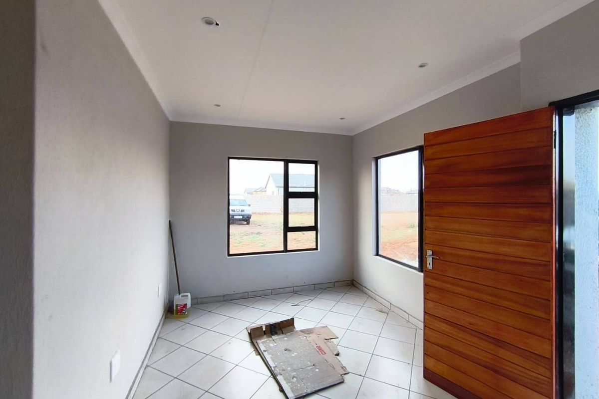 A bright, empty bedroom featuring neutral grey walls, tiled flooring, recessed ceiling lighting, and a modern horizontal-slat wooden door.