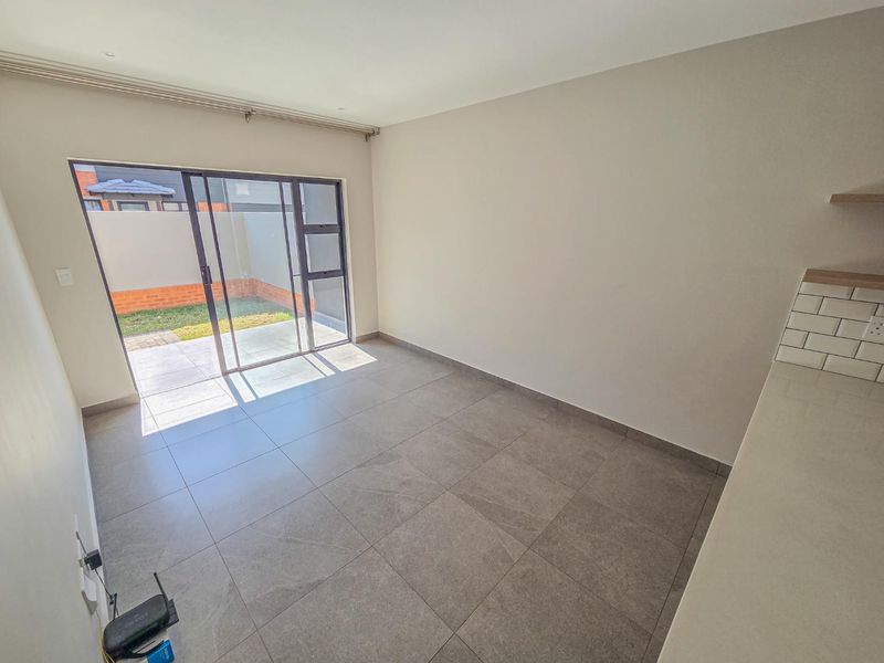 An open-plan living area featuring large format floor tiles, a modern kitchen corner with subway tile backsplash, and sliding doors leading to a private patio.