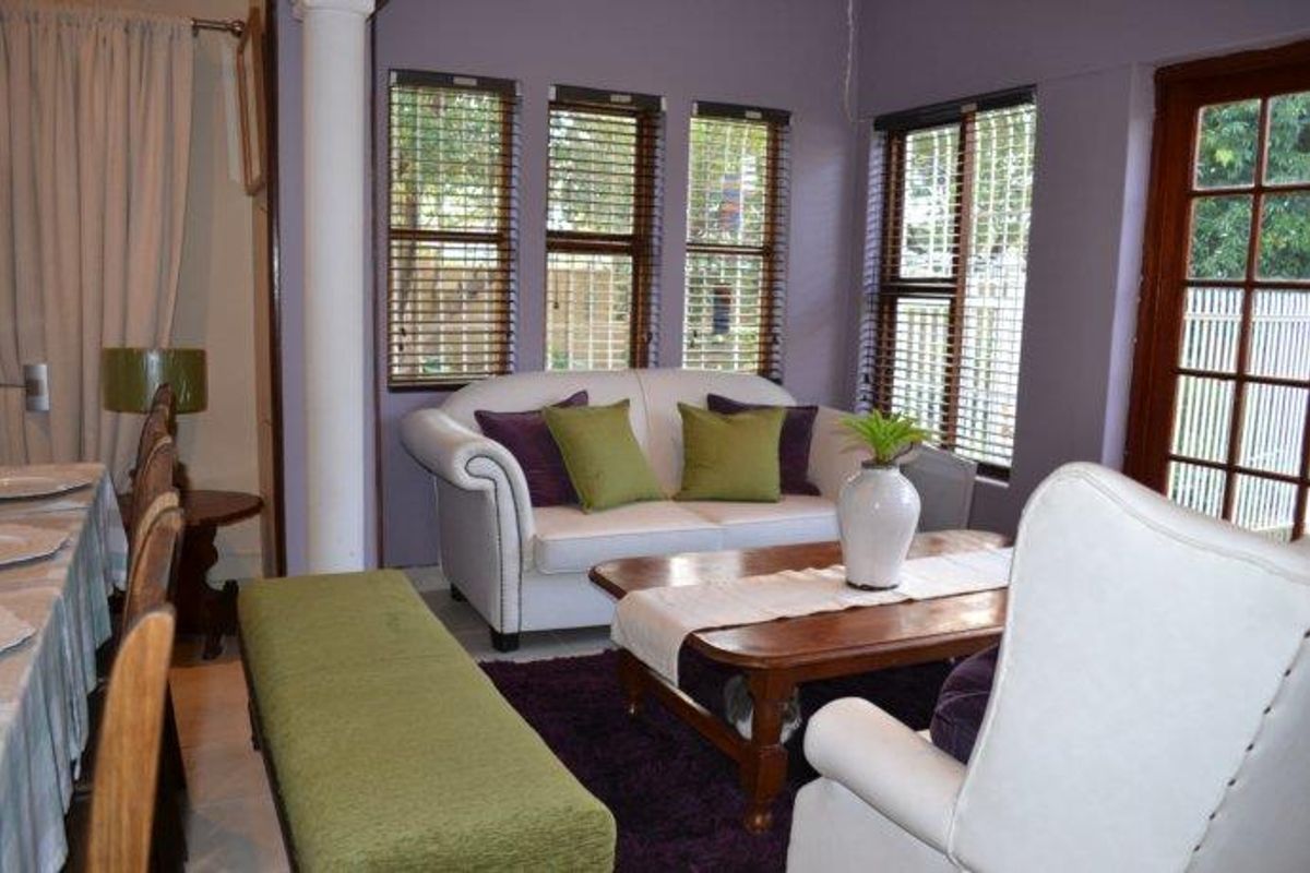 A living area featuring large windows with wooden blinds, a structural column, and access to an outdoor space through a timber-framed glass door.