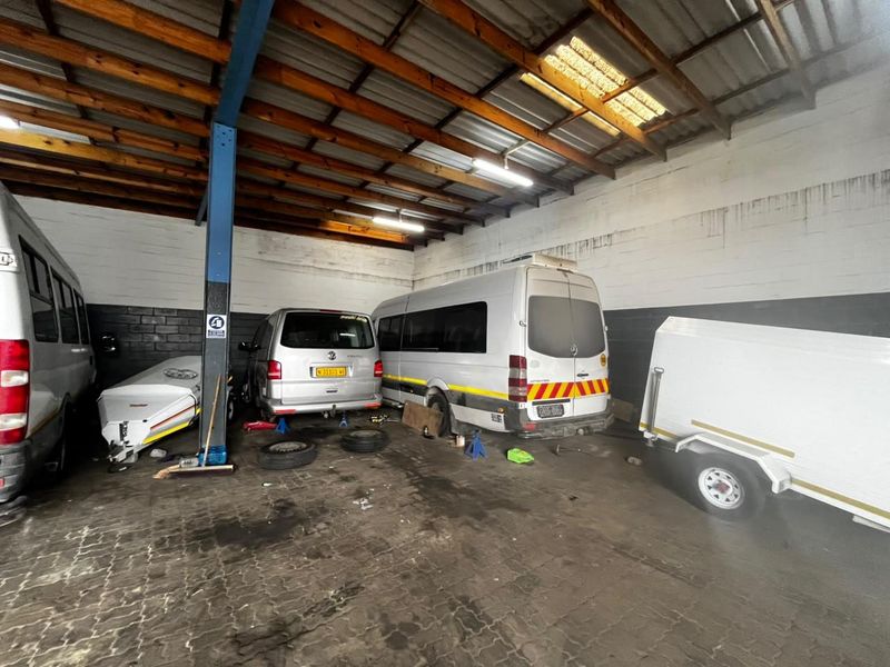 Spacious industrial garage featuring exposed timber roof trusses, painted concrete block walls, and durable paved flooring, suitable for vehicle maintenance or storage.