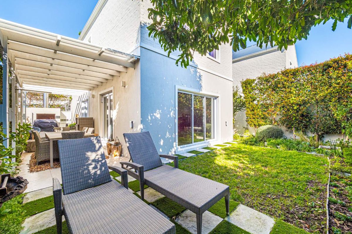 A well-maintained rear garden featuring a covered patio area, paved pathways, and established landscaping, providing a private outdoor living space.