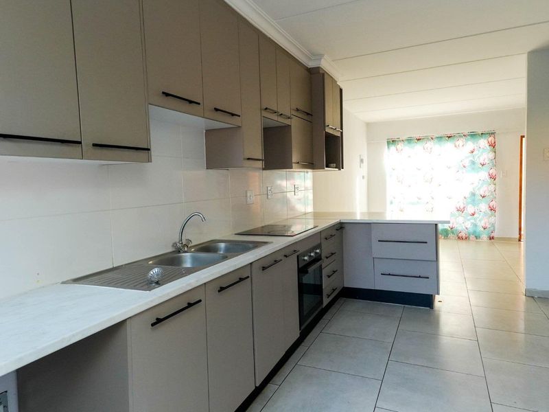 Modern kitchen featuring neutral cabinetry, integrated oven and hob, stainless steel double sink, and tiled flooring, flowing into an open-plan living area.