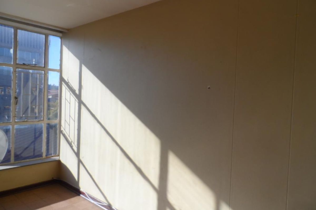 A vacant bedroom featuring large windows with security bars, tiled flooring, and plain wall finishes, offering a bright and blank canvas for renovation.